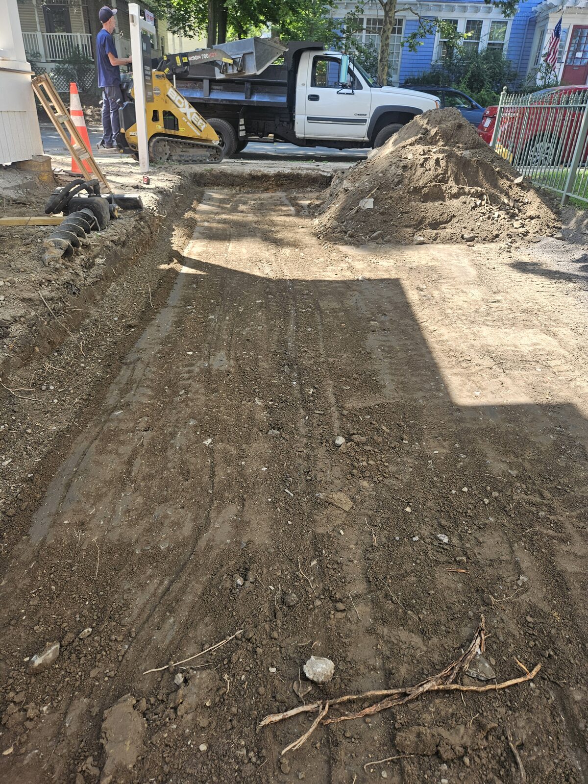 Excavated permeable driveway on Sycamore Street in Somerville, MA, with a compact track loader and dump truck, dug down to subgrade